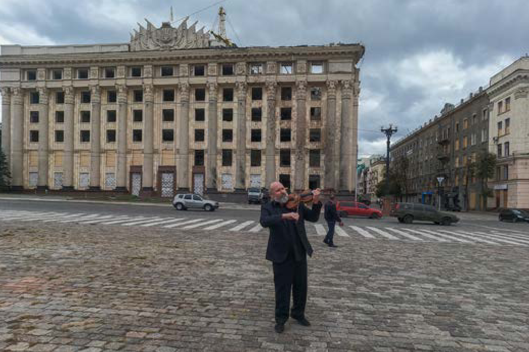 Харків, чоловік грає на скрипці на фоні зруйнованої будівлі ХОВА